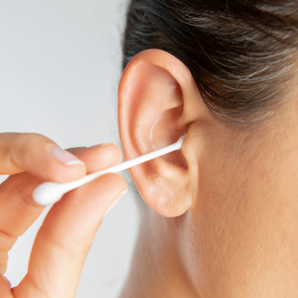 A person cleaning their ear with a cotton swab, close-up on the ear and swab with a blurred background.