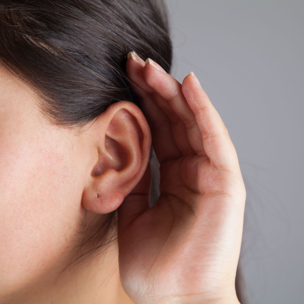A person cupping their hand behind their ear to listen.