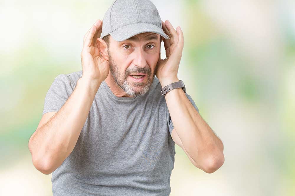 Man in a gray cap cupping his hands around his ears to hear, as when one hearing aid sounds weaker, from Staverman Hearing Centers in Jacksonville, FL